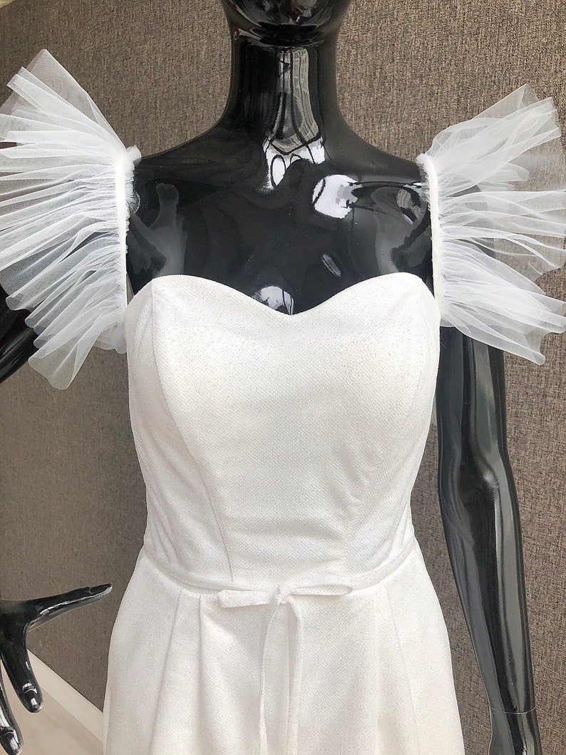 K&ouml;nnte beinhalten: Wei&szlig;er Festtags-Jumpsuit mit herzf&ouml;rmigem Ausschnitt und zarter Schleife in der Taille. Der Jumpsuit hat transparente, ger&uuml;schte &Auml;rmel. Der Stoff hat eine subtile Textur, die einen raffinierten Look erzeugt.