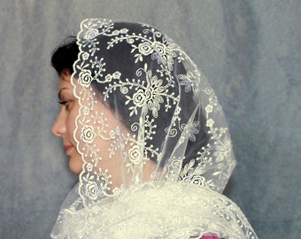May include: White lace veil with floral embroidery. The veil is sheer and has a scalloped edge. It is worn over a woman's head and shoulders.
