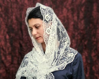 May include: A white lace veil with floral embroidery and a beaded fringe. The veil is draped over a person's head and shoulders.