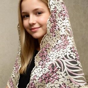 May include: A sheer, floral-patterned head covering in cream, pink, and gold tones. The delicate lace design features small flowers and swirling patterns. The head covering is draped over the head and shoulders.