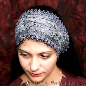 May include: A woman wearing a gray and silver lace headband with a delicate floral pattern. The headband is worn over her dark hair and covers her forehead.