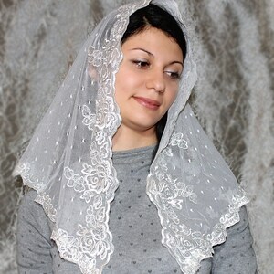 May include: A white lace veil with a delicate floral pattern. The veil is sheer and has a scalloped edge.