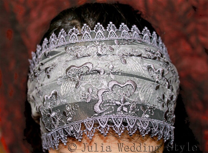 May include: A delicate, gray lace veil with a scalloped edge. The veil is made of a sheer fabric with intricate floral embroidery.