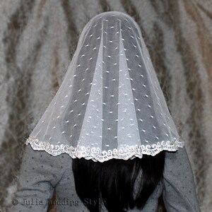 May include: White bridal veil with a dotted pattern and a silver lace trim. The veil is folded in a way that creates a dome shape.