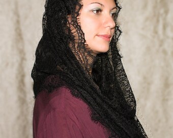 May include: A black lace mantilla, a traditional head covering, worn by a person with dark hair. The lace is delicate and intricate, with a scalloped edge.