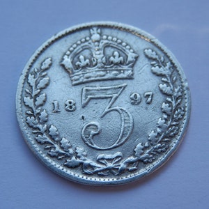 May include: Silver three pence coin from 1897 with a crown and wreath design.