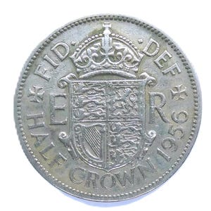 Può includere: Una moneta Half Crown d'argento del 1956, con un dettagliato stemma reale sotto una corona. La moneta presenta testo sul bordo, tra cui "HALF CROWN" e "1956".