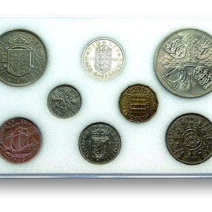 May include: A collection of eight British coins in a clear plastic case. The coins are arranged in two rows of four. The coins are all silver in color, except for one gold coin. The coins are all from the reign of Queen Elizabeth II.