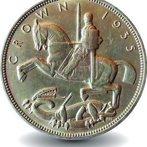 Puede incluir: Una moneda Crown de 1935 de tono plateado con un diseño en relieve de San Jorge a caballo empuñando una espada, posicionado sobre un dragón. El texto CROWN 1935 está inscrito a lo largo del borde superior de la moneda circular con borde perlado.