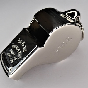 Peut inclure: Un sifflet argenté avec une inscription noire qui dit "The Acme Thunderer Made in England" et un anneau argenté avec une inscription noire qui dit "C.W.R."