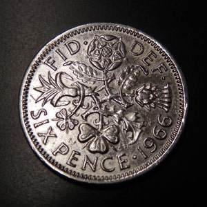 Może przedstawiać: Srebrna moneta sześciopeniowa z 1966 roku z napisem "FID DEF" i "SIXPENCE" wokół krawędzi. Na monecie widnieje róża, oset i koniczyna.