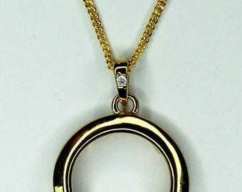 Könnte beinhalten: Goldfarbene Halskette mit Anhänger, der einen kreisförmigen Rahmen aufweist. Der Anhänger hängt an einer filigranen Kette. Ein kleiner, klarer Edelstein ist in der Öse gefasst. Die Halskette wird vor weißem Hintergrund gezeigt.