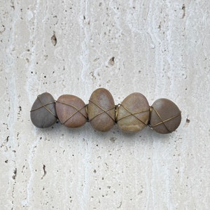 May include: Five brown stones wrapped with wire, arranged in a row. The stones are different sizes and shapes, and the wire is wrapped around them in a criss-cross pattern.