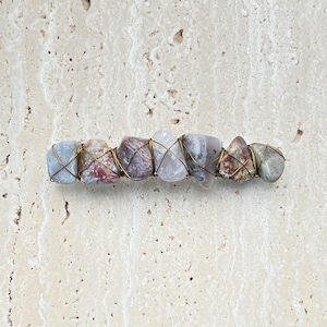 May include: A hair clip made of natural stones wrapped in wire. The stones are a mix of gray, white, and brown. The wire is a brass color.