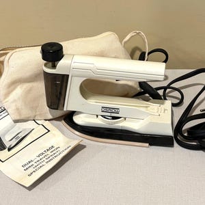 May include: A white and black mini travel iron with a black power cord, a beige carrying case, and an instruction manual. The iron has the brand name "OSROW" printed on it. The instruction manual reads "DUAL-VOLTAGE MINI TRAVEL IRON (WITH SPRAY)".