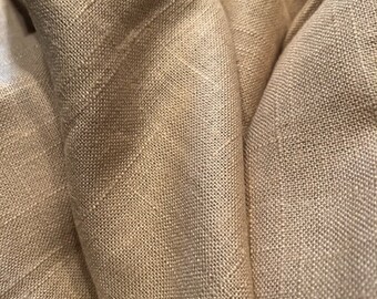 May include: A close-up of a beige linen fabric with a textured weave. The fabric is folded and draped, showing the soft, natural texture.