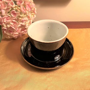 May include: A black and white speckled ceramic teacup and saucer set. The cup has a white interior and the saucer has a black rim.