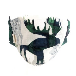 May include: A white face mask with a green and black plaid moose design. The moose is silhouetted against a white background with small grey floral patterns.