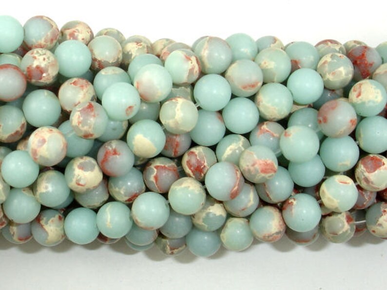May include: A strand of round, light blue and white jasper beads with red and brown marbling. The beads are approximately 8mm in diameter.