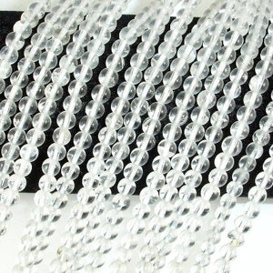 May include: A strand of clear quartz beads, each bead is round and smooth. The beads are strung together on a clear thread.