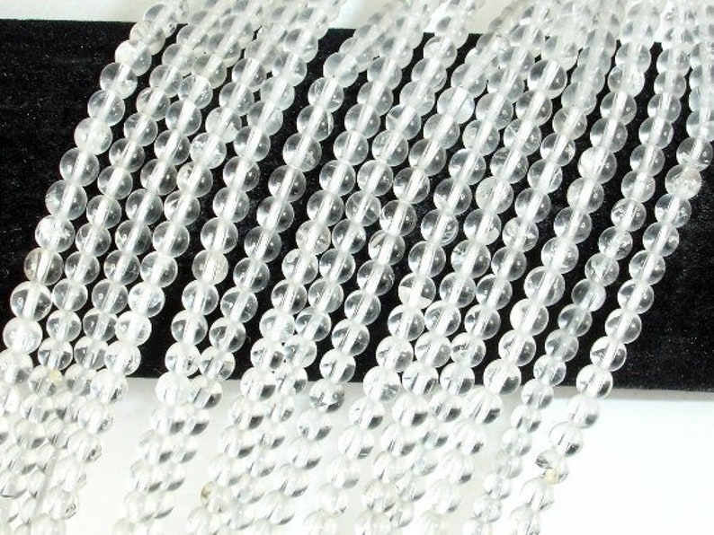May include: A strand of clear quartz beads, each bead is round and smooth. The beads are strung together on a clear thread.