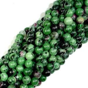 May include: A strand of green, black, and pink gemstone beads. The beads are round and have a speckled appearance.