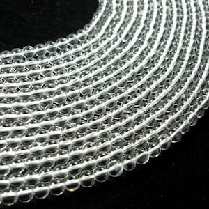 May include: A strand of clear glass beads, arranged in a circular pattern. The beads are smooth and translucent, with a slight shimmer.