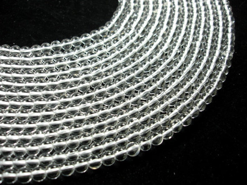 May include: A strand of clear glass beads, arranged in a circular pattern. The beads are smooth and translucent, with a slight shimmer.