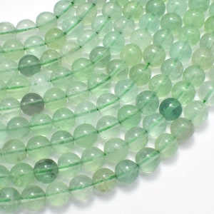 May include: A strand of light green gemstone beads. The beads are round and smooth, and they have a translucent appearance. The beads are strung on a clear thread.