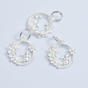 Peut inclure: Trois breloques en argent en forme de cercle avec un lapin à l'intérieur. Les breloques sont décorées de petites fleurs sur le bord.