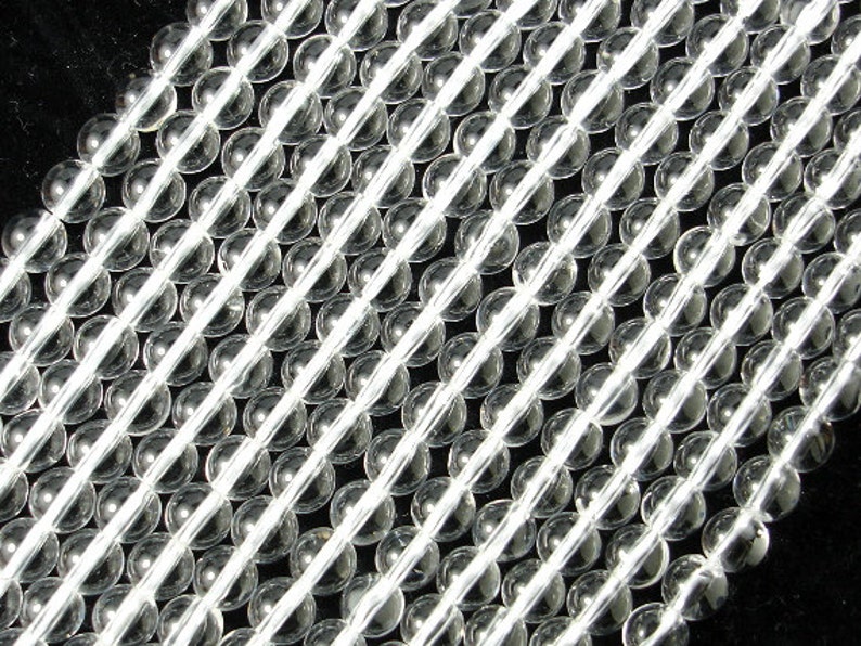 May include: A strand of clear glass beads, arranged in rows. The beads are round and smooth, with a slight shine.