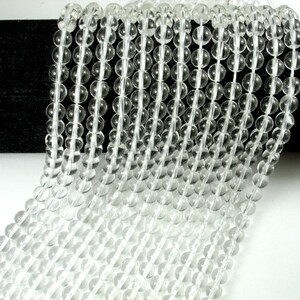 May include: A strand of clear quartz crystal beads. The beads are round and smooth, and they are strung on a clear thread. The beads are all approximately the same size.