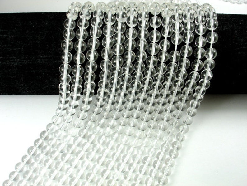 May include: A strand of clear quartz crystal beads. The beads are round and smooth, and they are strung on a clear thread. The beads are all approximately the same size.