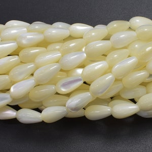 May include: A strand of white pearlescent teardrop-shaped beads. The beads are smooth and have a subtle iridescent sheen.