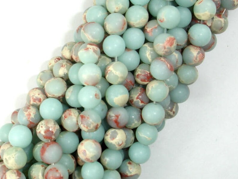 May include: A strand of round, light blue and white marbled gemstone beads. The beads have a mottled, speckled appearance with hints of red.