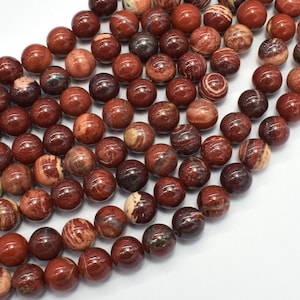 May include: A strand of red jasper beads with white and brown swirls. The beads are round and smooth, and they are strung on a clear thread.