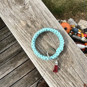May include: A light blue crocheted key chain with a silver ring and a maroon tassel.