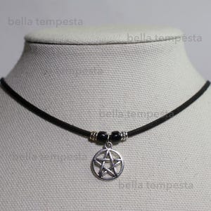 May include: A black choker necklace with a silver pentagram pendant. The necklace is made of a thin black cord and has two black beads on either side of the pendant.