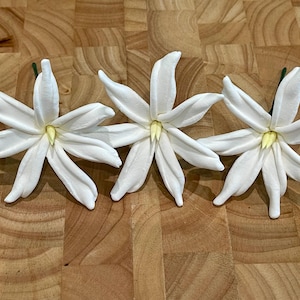 以下が含まれることがあります： 木製の表面に並んだ、黄色の芯を持つ白い砂糖の花が3つ