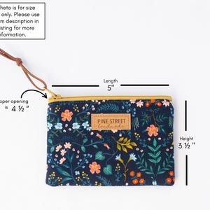May include: A navy blue floral print pouch with a gold zipper and a leather wrist strap. The pouch is 12.7 cm long and 8.9 cm high. The zipper opening is 11.4 cm. The label reads "PINE STREET handmade."