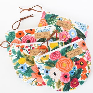 May include: Four floral print pouches with leather zipper pulls. The pouches feature a white background with colorful flowers in shades of red, pink, orange, and blue. Each pouch has a leather tag that reads "PINE STREET handmade".