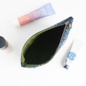 Peut inclure: Une pochette zipp&eacute;e bleu fonc&eacute; &agrave; motif floral avec une doublure int&eacute;rieure vert citron. La pochette est ouverte et vide, plac&eacute;e &agrave; c&ocirc;t&eacute; d'un tube de lotion corporelle Lavender Moon, d'un petit tube blanc de cr&egrave;me pour les mains et d'un flacon.
