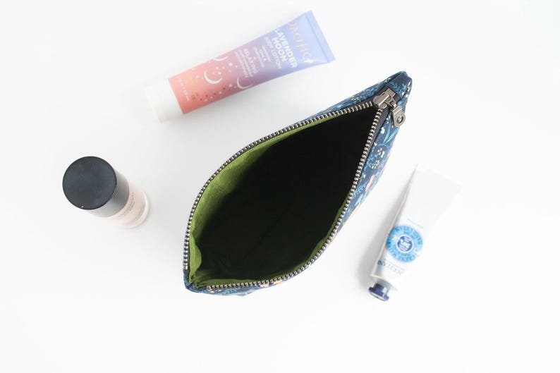 Peut inclure: Une pochette zipp&eacute;e bleu fonc&eacute; &agrave; motif floral avec une doublure int&eacute;rieure vert citron. La pochette est ouverte et vide, plac&eacute;e &agrave; c&ocirc;t&eacute; d'un tube de lotion corporelle Lavender Moon, d'un petit tube blanc de cr&egrave;me pour les mains et d'un flacon.