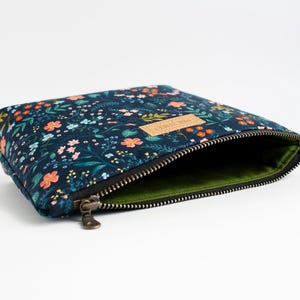 Peut inclure: Une pochette zipp&eacute;e bleu fonc&eacute; avec un motif floral color&eacute; compos&eacute; de petites fleurs orange, roses et bleu clair ainsi que de feuilles vertes. La pochette poss&egrave;de une fermeture &eacute;clair en m&eacute;tal, une doublure vert olive et une &eacute;tiquette beige PINE STREET.