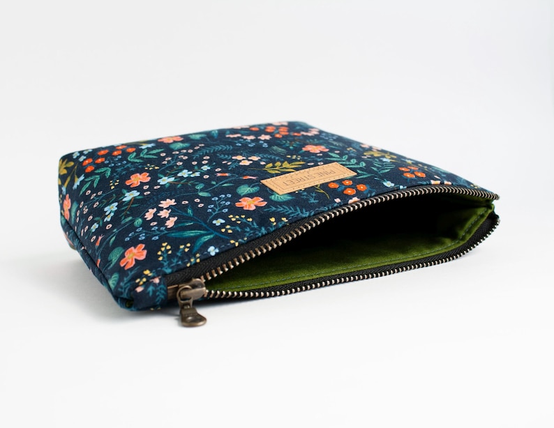 Peut inclure: Une pochette zipp&eacute;e bleu fonc&eacute; avec un motif floral color&eacute; compos&eacute; de petites fleurs orange, roses et bleu clair ainsi que de feuilles vertes. La pochette poss&egrave;de une fermeture &eacute;clair en m&eacute;tal, une doublure vert olive et une &eacute;tiquette beige PINE STREET.