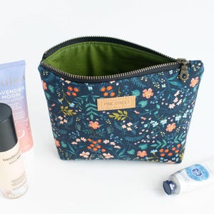 Peut inclure: Une pochette zipp&eacute;e bleu fonc&eacute; avec un motif floral color&eacute;, dot&eacute;e d'une &eacute;tiquette en cuir beige gaufr&eacute;e avec le texte PINE STREET. La pochette poss&egrave;de une doublure int&eacute;rieure vert olive et est accompagn&eacute;e d'une lotion et deux tubes de cr&egrave;me.