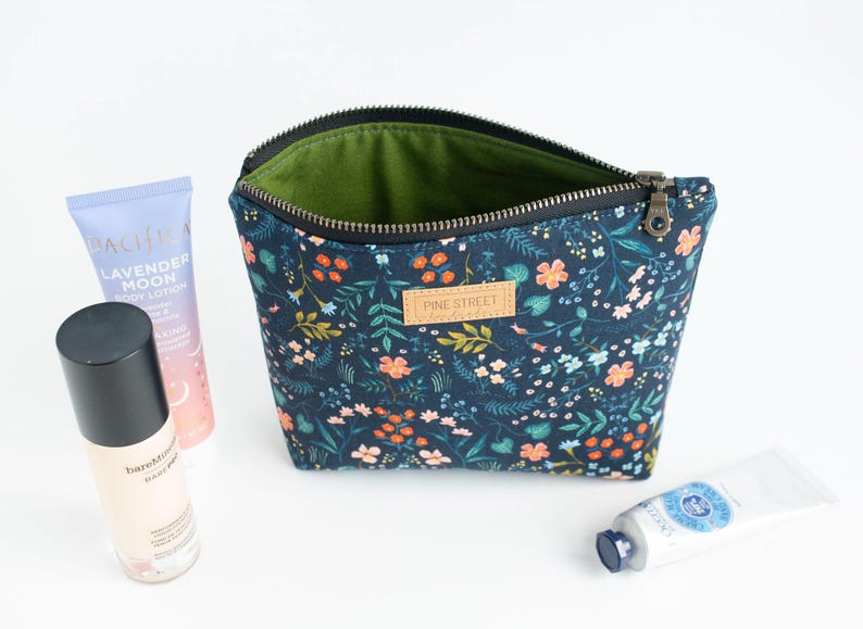 Peut inclure: Une pochette zipp&eacute;e bleu fonc&eacute; avec un motif floral color&eacute;, dot&eacute;e d'une &eacute;tiquette en cuir beige gaufr&eacute;e avec le texte PINE STREET. La pochette poss&egrave;de une doublure int&eacute;rieure vert olive et est accompagn&eacute;e d'une lotion et deux tubes de cr&egrave;me.