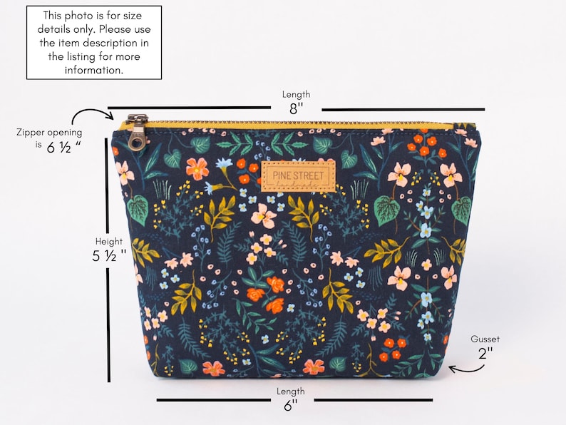 May include: A dark blue zippered pouch with a floral print. The pouch measures 8 inches long, 6 inches wide, and 5 1/2 inches tall. The zipper opening is 6 1/2 inches wide. The pouch has a gusset of 2 inches. The pouch has a brown leather label with the text "PINE STREET".