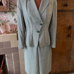 Puede incluir: Un traje de falda a cuadros verde y blanco con una chaqueta entallada y una falda hasta la rodilla. La chaqueta tiene un cuello puntiagudo y un cierre de un solo botón. La falda tiene una silueta recta.