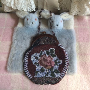 Può includere: Una borsa vintage di perline con un design floreale. La borsa è rotonda e ha una chiusura marrone. La borsa è realizzata con perline marroni scure, nere e bianche.